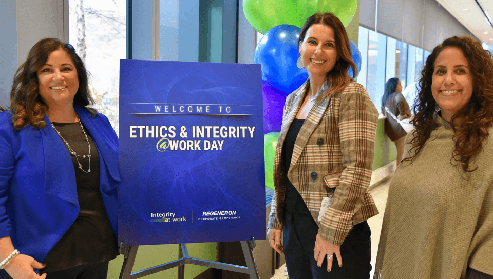 Two Regeneron employees posing next to a sign that reads 'Welcome to Ethics & Integrity at Work Day'.